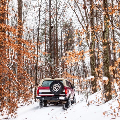 1995 Ford Bronco - A 1995 Ford Bronco navigates a snow-covered path through a forest with bare trees.