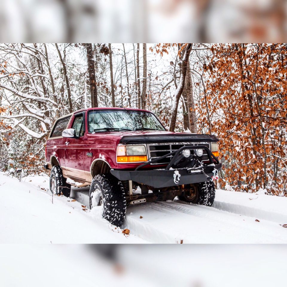 Red 1995 Ford Bronco with aftermarket bumper and lights driving in snow