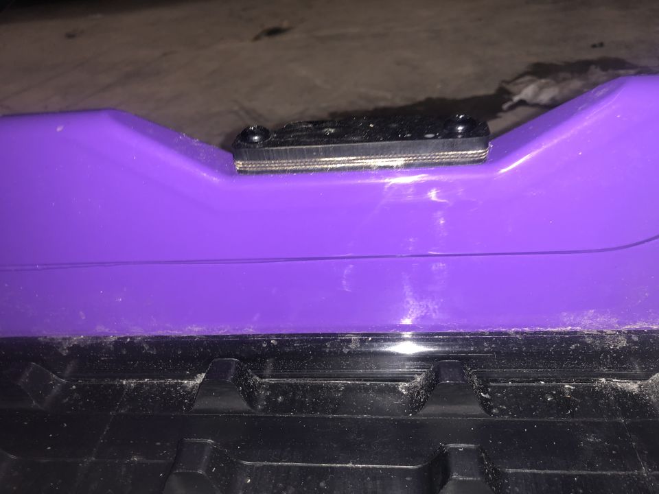Purple snowmobile body panel with a black mounting bracket attached. The panel has a textured black track visible below it
