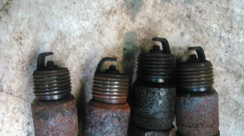 1991 Ford F-150 - A set of four spark plugs, showing signs of wear and rust, with a Supermotors.net watermark visible.