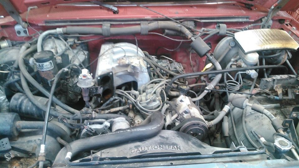 Engine bay with hoses, wires, and engine components visible. 'CAUTION FAN' text on a black shroud