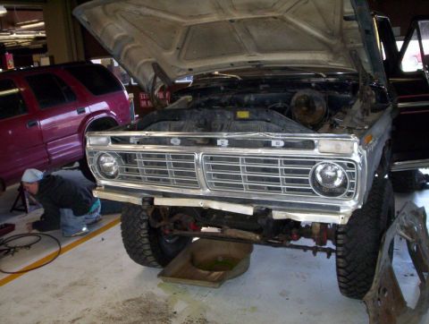 1978 Ford Bronco - A 1978 Ford Bronco is shown with its hood open, revealing the engine bay and front grille, with another vehicle and a mechanic in the backg…