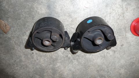 1993 Mazda MX-3 - Two engine mounts are shown on a concrete floor, possibly for a Mazda vehicle.