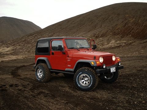 1996 Ford Bronco - Red Jeep Wrangler TJ parked on a dirt road with barren hills in the background.