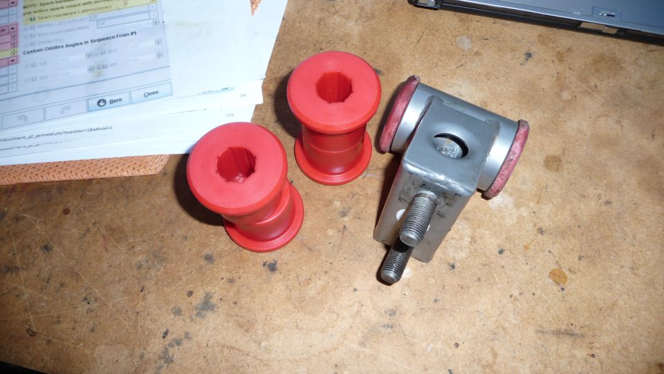 Three red polyurethane bushings and one metal bracket with red inserts on a wooden surface