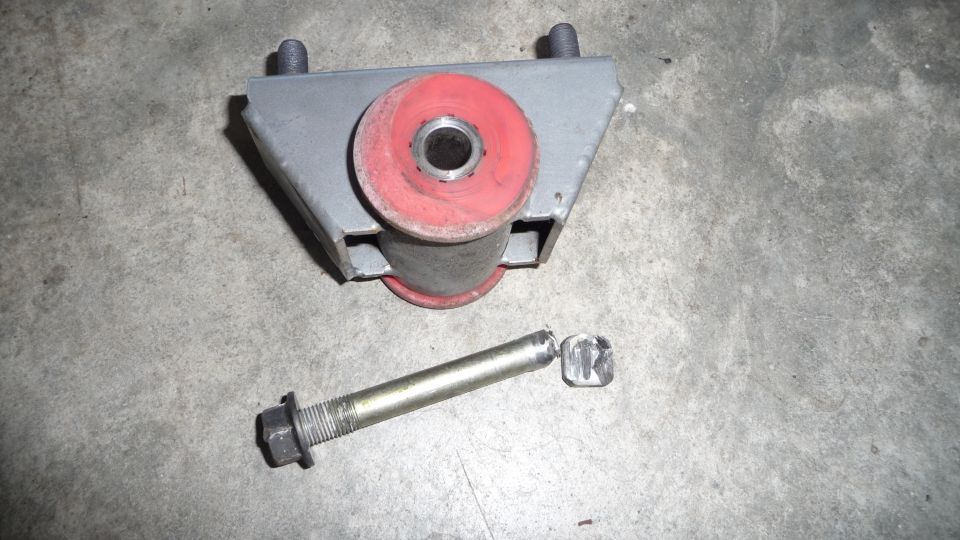 Engine mount with red bushings and a separate bolt on a concrete surface