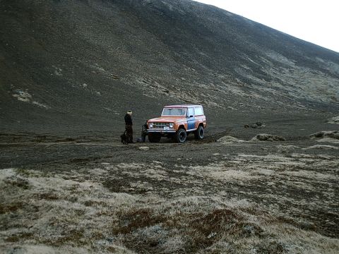 1996 Ford Bronco - A person stands next to an orange and blue SUV in a desolate, rocky landscape.
