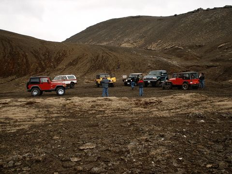 1996 Ford Bronco - Several off-road vehicles are gathered in a desolate, hilly landscape under an overcast sky.