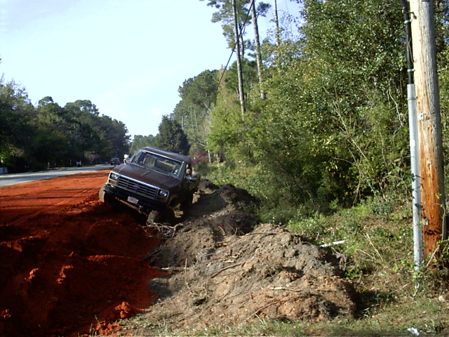 1985 Ford Bronco stuck in a dirt embankment next to a road