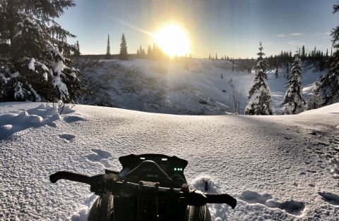 2019 Arctic Cat Mountain Cat 800 - View from a snowmobile dashboard as the sun sets over a snow-covered mountain landscape.