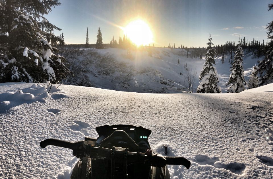 Snowmobile handlebars and dashboard with Arctic Cat logo, set against a snowy landscape at sunset