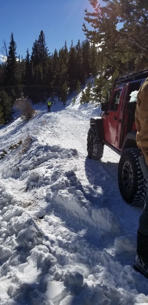 1996 Ford Bronco - A red Jeep Wrangler navigates a snow-covered mountain road with a person in the distance.