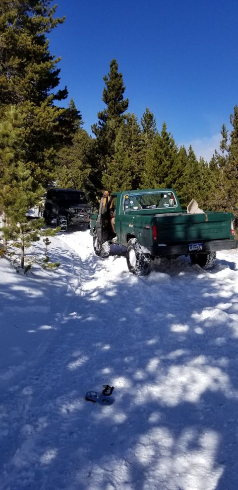 1996 Ford Bronco - A green pickup truck navigates a snowy path, with a dark SUV following behind in a wooded area.