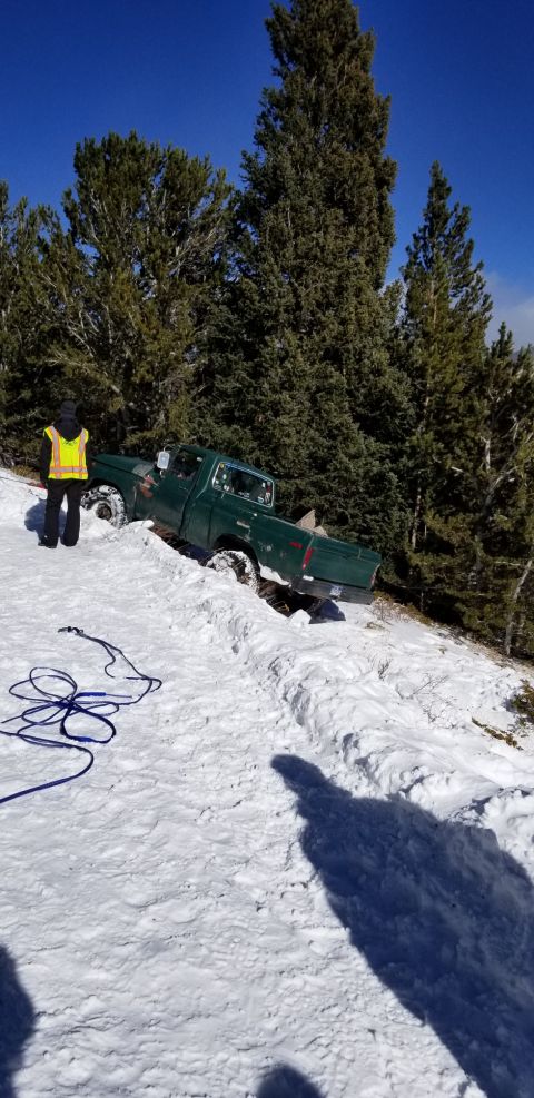 1996 Ford Bronco - A green pickup truck is stuck in a snowy ditch on a hillside, with a person in a safety vest standing nearby.