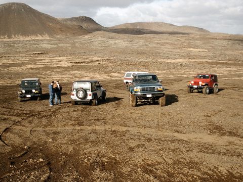 1996 Ford Bronco - Several off-road vehicles are parked in a desolate, mountainous terrain under a cloudy sky.