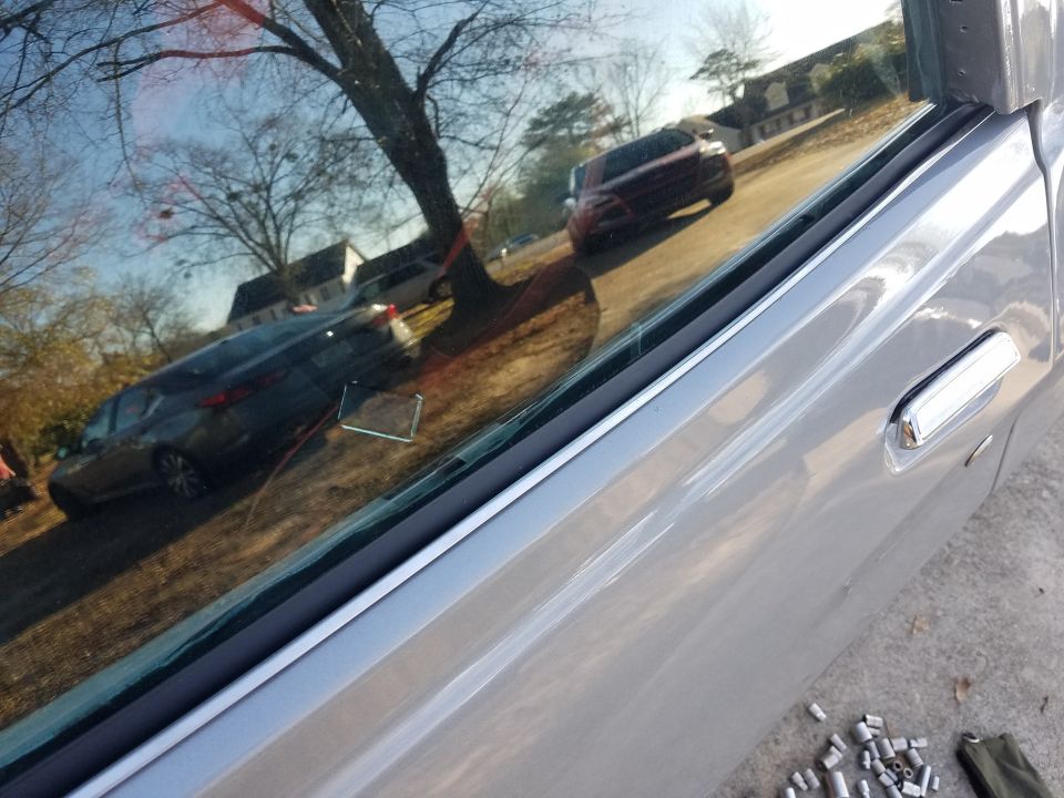 Reflection of two cars and houses in a car window, with a tree in the foreground