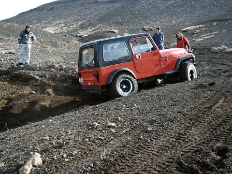 1996 Ford Bronco - A red Jeep Wrangler navigates a challenging, rocky landscape with three people observing.