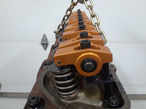 1985 Ford Bronco - Close-up of an engine's valve train components, including rocker arms and springs, being lifted by a chain hoist.