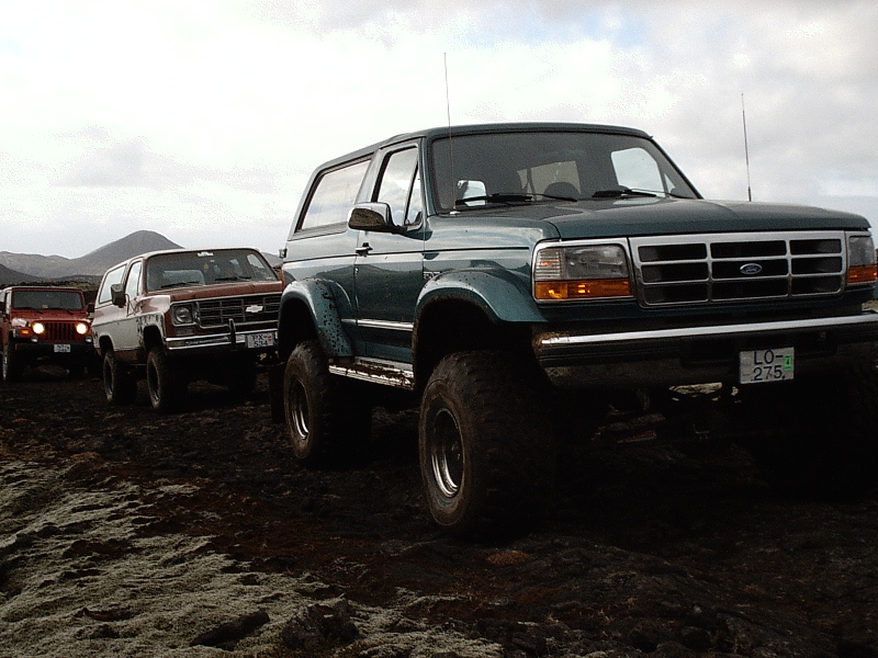 Lifted teal Ford Bronco on big tires with Chevy Blazer and Jeep behind on rocky terrain