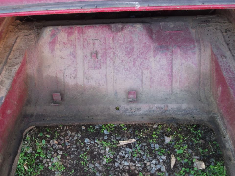 Red car trunk interior with dirt and gravel visible at the bottom