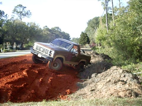 1985 Ford Bronco - A brown 1980s Ford Bronco navigates a challenging dirt terrain, with its front wheels angled upwards.