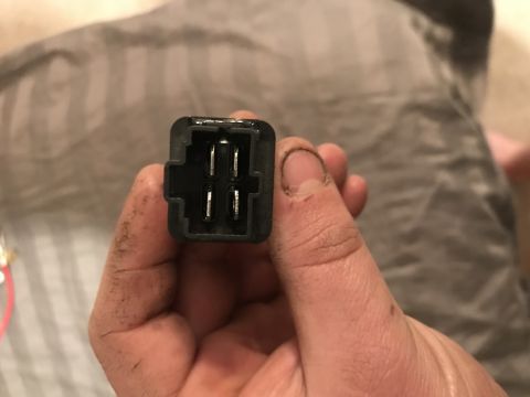 1995 Ford Bronco - A hand holds a black electrical connector with four visible metal pins, likely a component from a vehicle's wiring system.