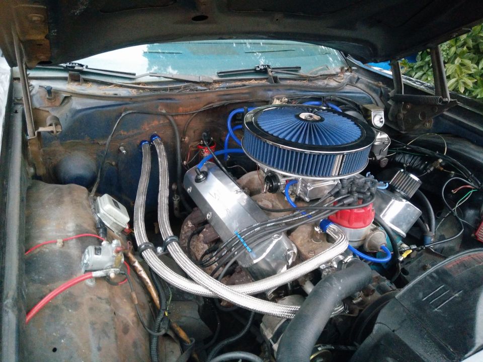 Close-up of a classic car engine bay with a blue air filter and chrome components.