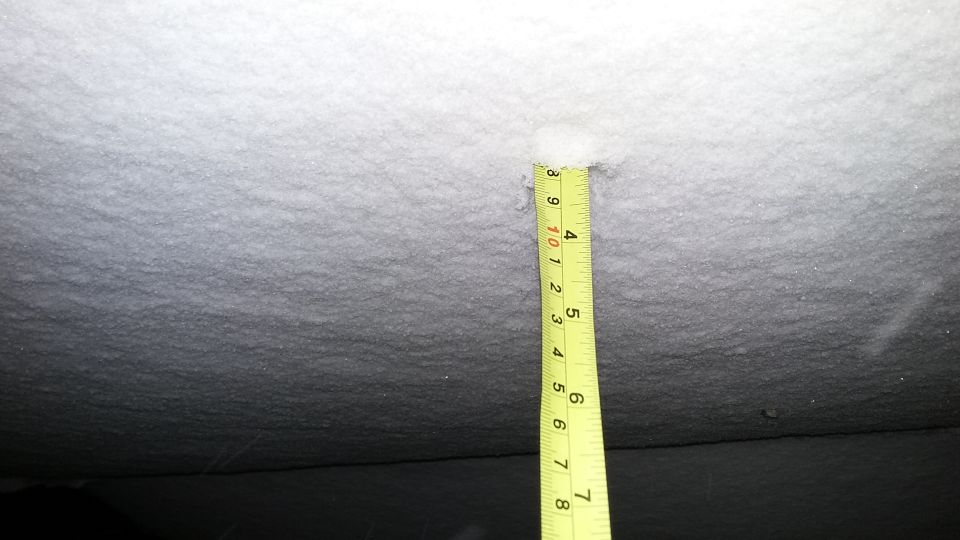 Yellow measuring tape in snow, showing depth of approximately 9.5 inches.