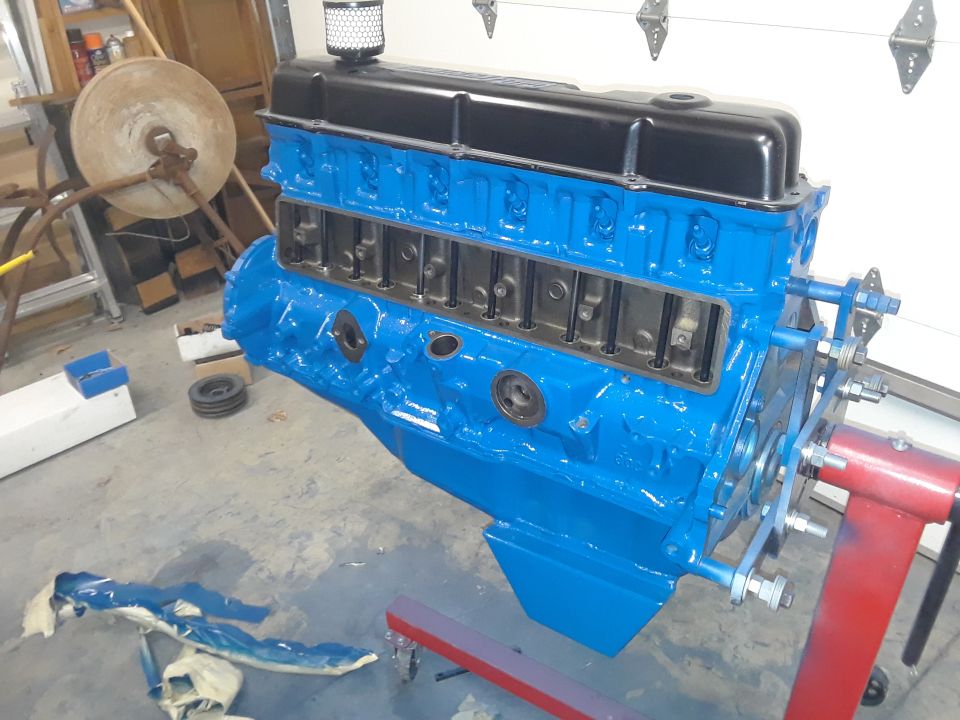 Blue engine block with black valve cover on a red engine stand in a garage.