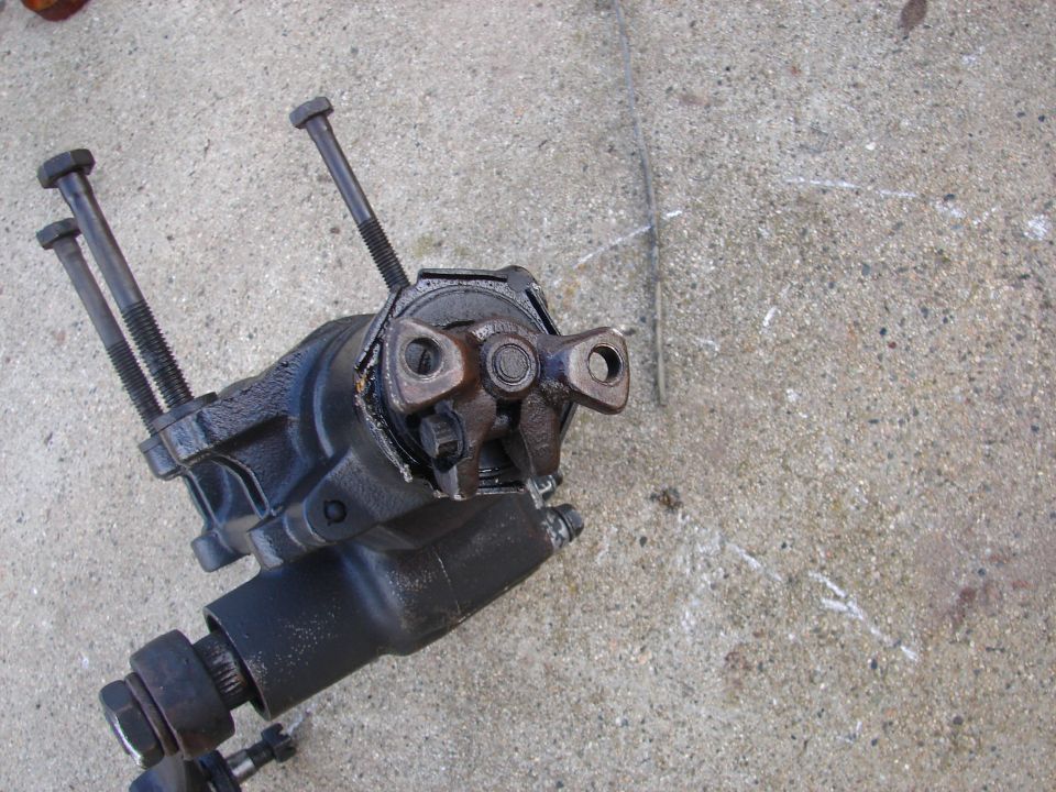 Black automotive steering gearbox with bolts and splined shaft on concrete.