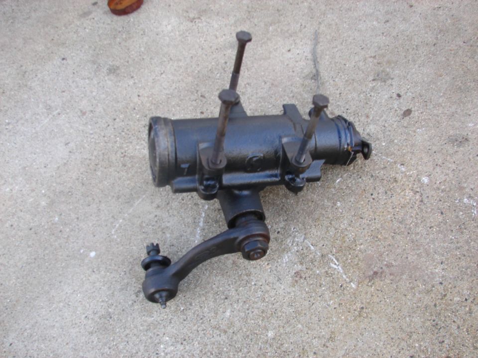 Black automotive steering gear box assembly with tie rod end on concrete.