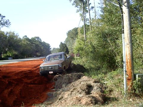 1985 Ford Bronco - A brown pickup truck is partially stuck in a dirt embankment next to a road.