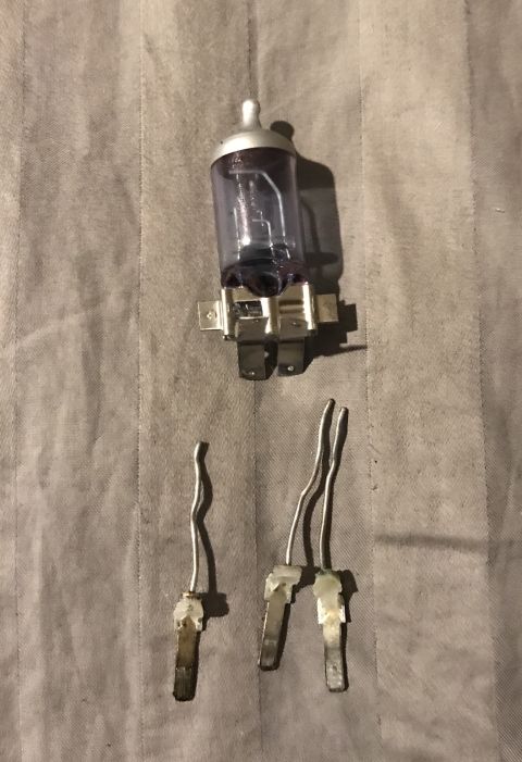 1995 Ford Bronco - Two automotive headlight bulbs are shown, one is a complete bulb with a clear glass enclosure and silver base, and the other is a disassemb…