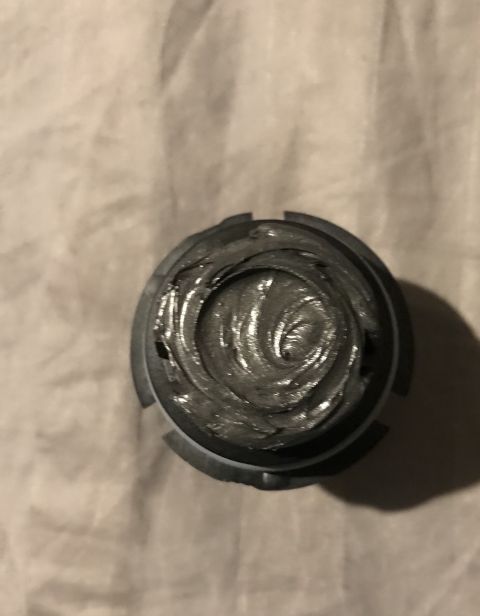 1995 Ford Bronco - A close-up, top-down view shows a dark gray, viscous grease packed into a metal cap with notches around its perimeter. The grease has a swi…