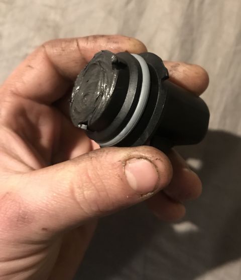 1995 Ford Bronco - A hand holds a black plastic part covered in gray grease. The part has two distinct rings around its circumference.