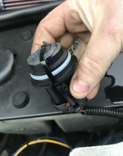 1995 Ford Bronco - A hand holds a black electrical connector with a rubber seal and a zip tie wrapped around it. The connector is part of a wiring harness vis…