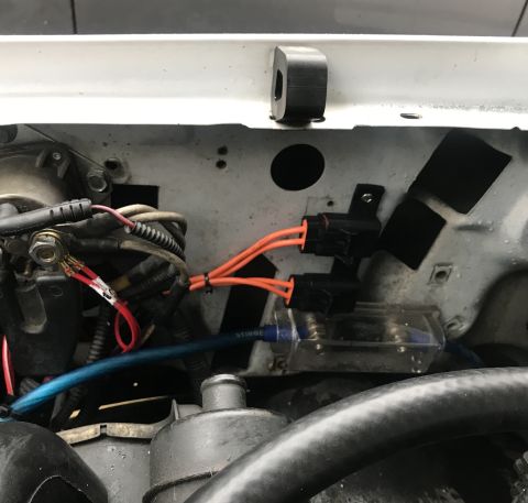 1995 Ford Bronco - A close-up view of aftermarket wiring and a fuse block installed in the engine bay of a vehicle. Orange wires connect to two black connecto…