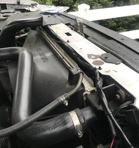1995 Ford Bronco - Close-up view of the engine bay of a 1995 Ford Bronco, focusing on the radiator fan shroud and hoses. The fan shroud has embossed text that…