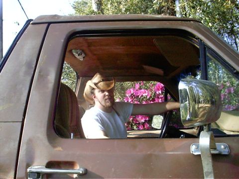 1985 Ford Bronco - A man wearing a cowboy hat is seen from the side, driving a 1985 Ford Bronco.