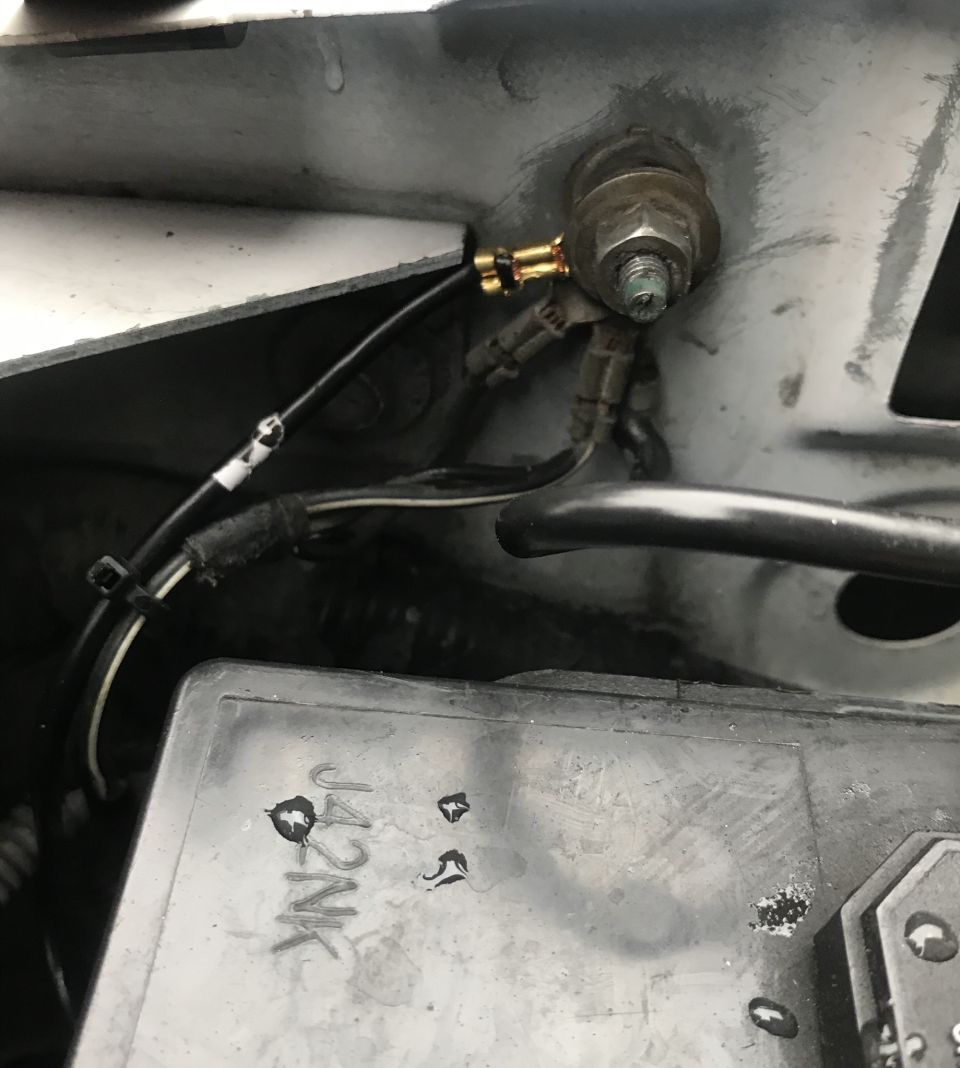Close-up of vehicle engine bay wiring, ground stud, and fuse box.