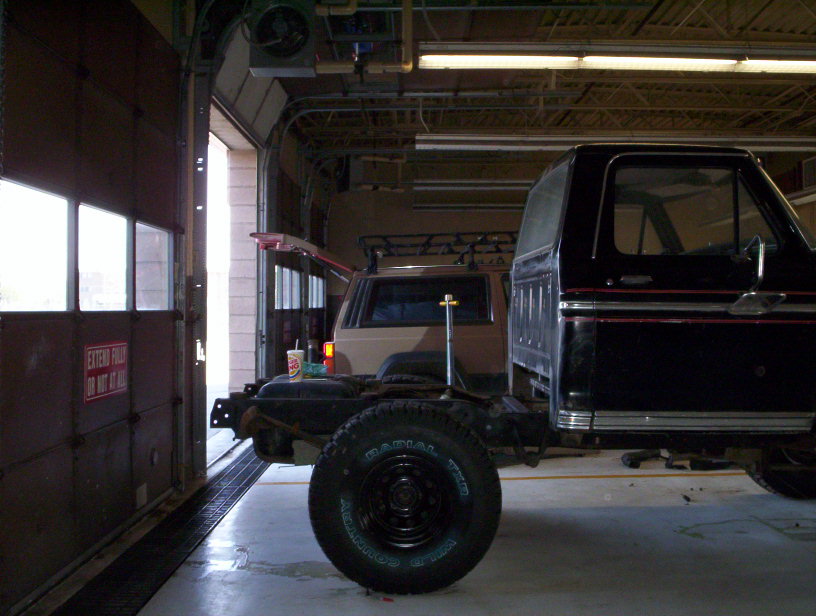Black Ford Bronco body on a chassis, another SUV behind it in a garage