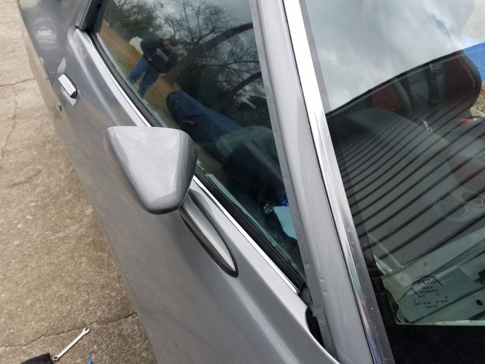 Gray car door and side mirror with a wrench on the ground.