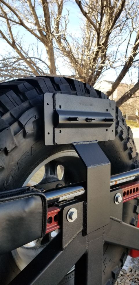 1996 Ford Bronco - A close-up view of a black, heavy-duty tire mount attached to the rear of a vehicle, likely an SUV, with a portion of a Hi-Lift jack visibl…