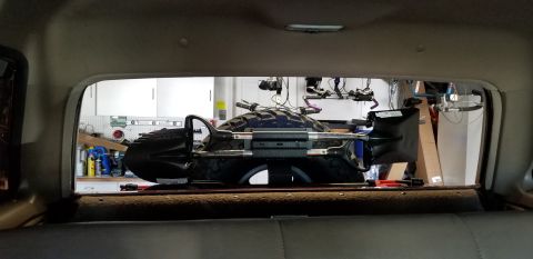 1996 Ford Bronco - View through the rear window of a vehicle showing a spare tire mounted with a shovel and axe attached. The background appears to be a garag…