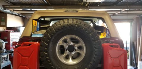 1996 Ford Bronco - The rear of a tan and maroon Ford Bronco is shown, equipped with a spare tire mounted on the tailgate, two red jerry cans, and two Kobalt t…
