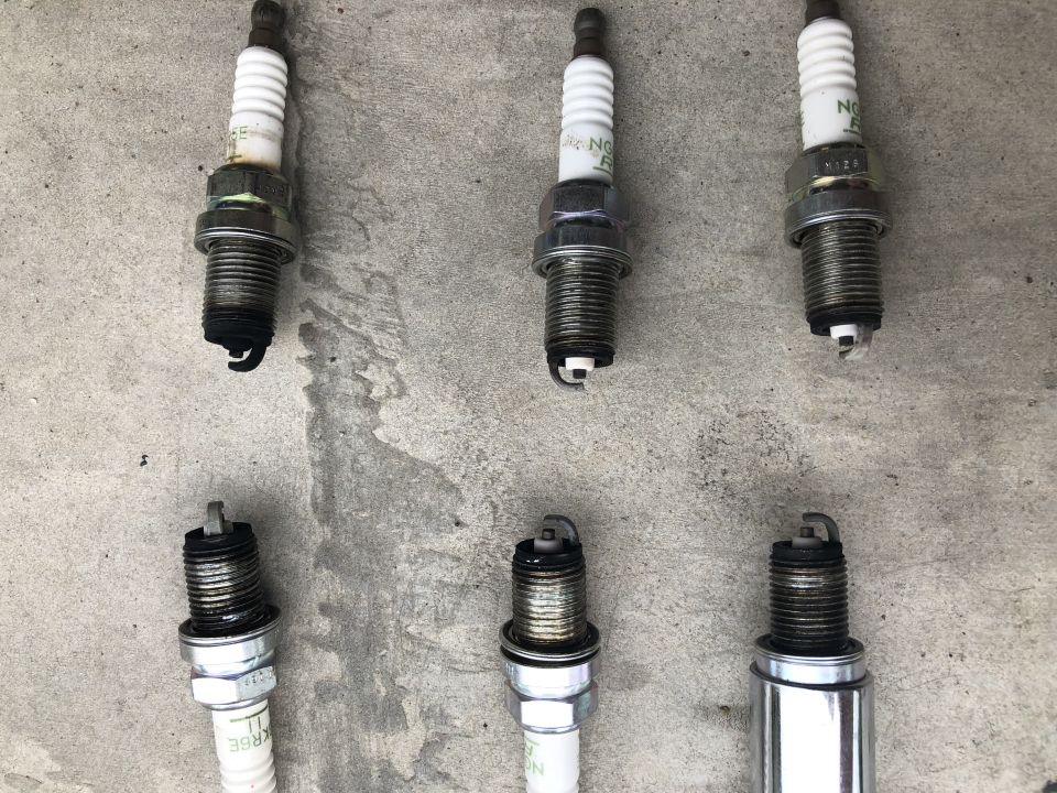 Six used spark plugs on a concrete surface.