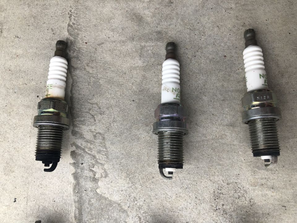 Three used NGK spark plugs on a concrete surface