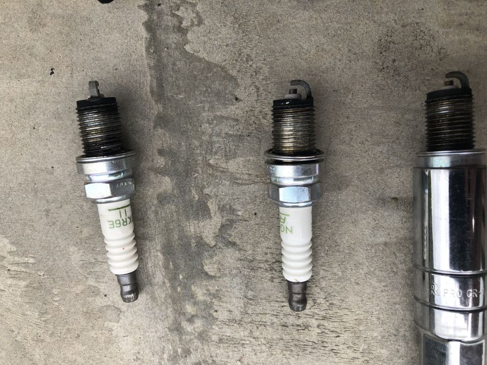 Three used spark plugs on a concrete surface.