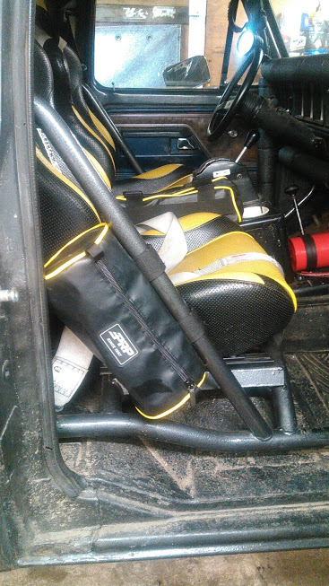 1978 Ford Bronco - Interior view of a modified vehicle, showing racing seats with yellow and black upholstery, a roll cage, and a black storage bag with yello…