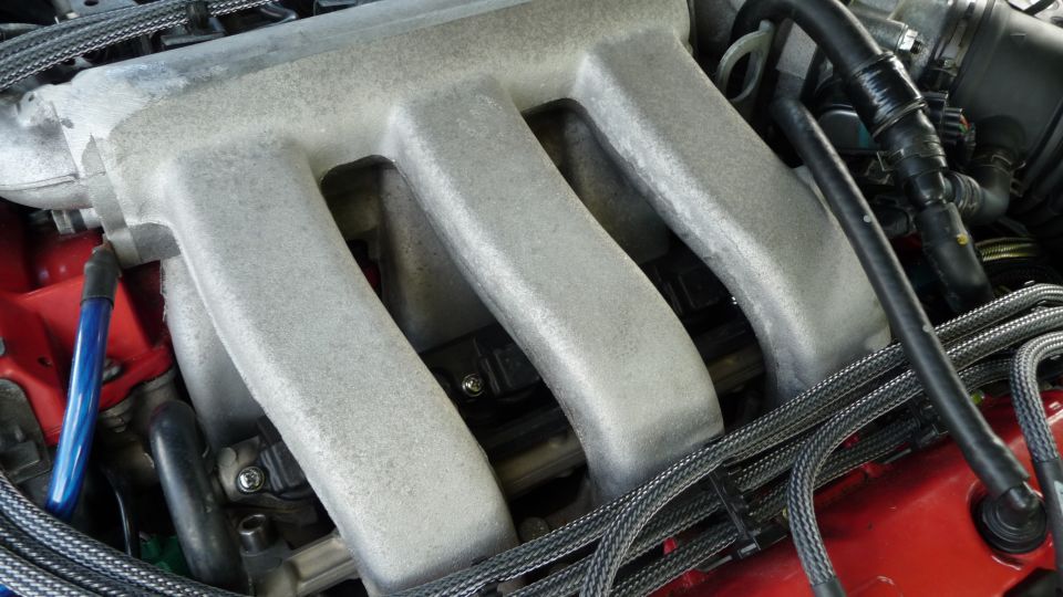 Close-up of a car's silver intake manifold with black hoses and wiring.